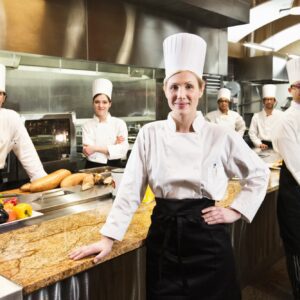 A portrait of a caucasian female chef and her team of chefs in the backgroiund.